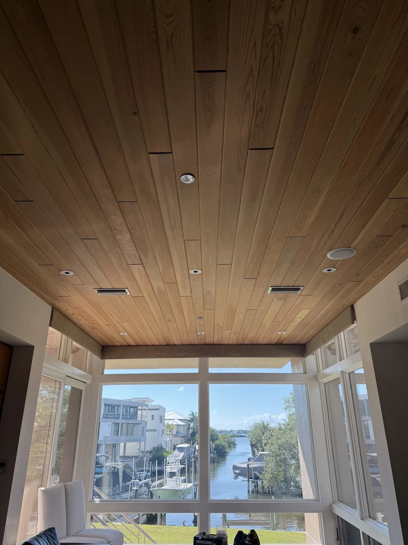Full room view of a wood ceiling with recessed lights, air vents and floor-to-ceiling glass